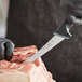 A hand in black gloves uses a Schraf curved flexible boning knife to cut meat on a counter.
