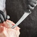 A person in black gloves uses a Schraf curved boning knife to cut up meat on a counter.