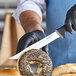 A person in a black glove using a Schraf serrated utility knife to cut a bagel.