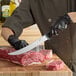 A person in gloves using a Schraf breaking knife to cut raw meat on a cutting board.