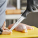 A person in black gloves uses a Schraf utility knife to cut chicken on a counter.