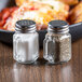 Two Tablecraft clear glass mini mason jar salt and pepper shakers with stainless steel tops on a table.