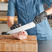 A person in a blue uniform and black gloves using a Schraf chef knife to cut meat.