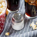 A Tablecraft clear glass salt shaker with a stainless steel top next to popcorn.