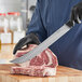 A man in gloves using a Schraf cimeter knife to cut meat on a wooden surface.