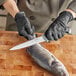 A person wearing black gloves filleting a fish with a Schraf flexible fillet knife.