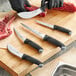 A Schraf butcher knife with a black handle cutting a piece of raw meat on a cutting board.