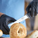 A person in black gloves cutting a sesame seed bagel with a Schraf serrated utility knife.