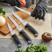 A person in black gloves uses a Schraf serrated utility knife to cut a tomato.