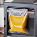 A VacPak-It vertical vacuum packaging machine sealing a bag of orange liquid.