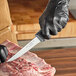 A person in black gloves using a Schraf boning knife to cut meat on a cutting board.