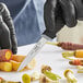 A person in black gloves uses a Schraf serrated paring knife to cut carrots.