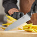 A person in black gloves using a Schraf chef knife to cut a yellow vegetable on a cutting board.