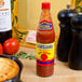 A bottle of The Original Louisiana Brand Hot Sauce on a table next to skillet cornbread and tomatoes.