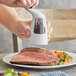 A hand using an OXO pepper grinder to add pepper to a plate of meat.