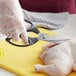 A person wearing gloves uses Mercer Culinary German steel shears to cut a chicken.