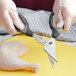 A person in gloves using Mercer Culinary German steel multi-purpose shears to cut a chicken.