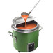 A green Vollrath stock pot with ladle pouring orange liquid into it.