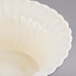 A Fineline Flairware ivory plastic bowl with a scalloped edge on a gray surface.