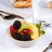 A Fineline Flairware ivory plastic bowl filled with fruit on a table.