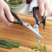 Mercer Culinary Japanese steel kitchen scissors cutting chives on a cutting board.