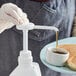 A person using a Tablecraft condiment pump to pour syrup on pancakes.