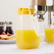 A Tablecraft dispenser jar filled with orange juice on a table next to a plate of pancakes and a glass of juice.