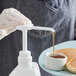 A gloved hand uses a Tablecraft syrup pump to pour syrup onto pancakes on a plate.