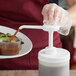 A person using a Tablecraft condiment pump to pour brown sauce into a white plastic container.