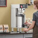 A woman using an Estella Caffe automatic single shuttle coffee maker to pour coffee.