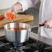 A person cooking cut carrots in a Choice aluminum sauce pan.