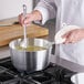 A chef cooking soup in a Choice tapered aluminum sauce pan.
