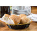 A Tablecraft black polypropylene oval bread basket with metallic gold trim filled with bread rolls on a table.