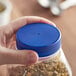 A hand holding a plastic container with a blue flat top induction-lined spice lid.
