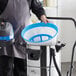 A person using a Lavex stainless steel wet/dry vacuum with blue and white plastic attachments.