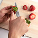 A person using a Shun Classic paring knife to cut strawberries on a cutting board.