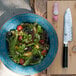 A bowl of salad next to a Shun Classic Santoku knife.