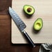 A Shun Classic Santoku knife next to a halved avocado on a cutting board.