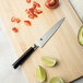 A Shun Classic Forged serrated utility knife on a cutting board with sliced avocados, tomatoes, lemons, limes.