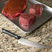 A Kai PRO curved boning and fillet knife next to a piece of raw meat on a tray.