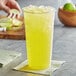 A tall clear plastic cup filled with yellow liquid and a slice of lemon on the rim.
