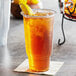 A clear Choice heavy weight plastic cup filled with iced tea and a lemon wedge.