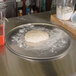 A dough ball on an American Metalcraft aluminum pizza pan on a counter.