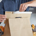 A person using a 16" handle cuff tamper evident bag seal to close a brown paper bag.