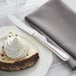 An Acopa Lydia stainless steel dessert knife on a plate with a piece of cake with whipped cream.