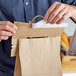 A man using a 10" Handle Cuff Tamper Evident Bag Seal on a brown paper bag.