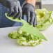 A person using a San Jamar green lettuce knife to cut lettuce.