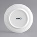 An Acopa Condesa white porcelain plate with scalloped edges and black text.