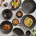 An Acopa Condesa matte gray porcelain plate with scalloped edges on a table with other plates of food and coffee.