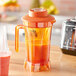 An AvaMix orange blender jar filled with orange liquid on a counter.